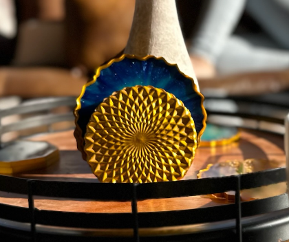 A close-up of a decorative gold and blue ceramic coaster or trivet with a textured sunburst pattern, resting on a round wooden tray.